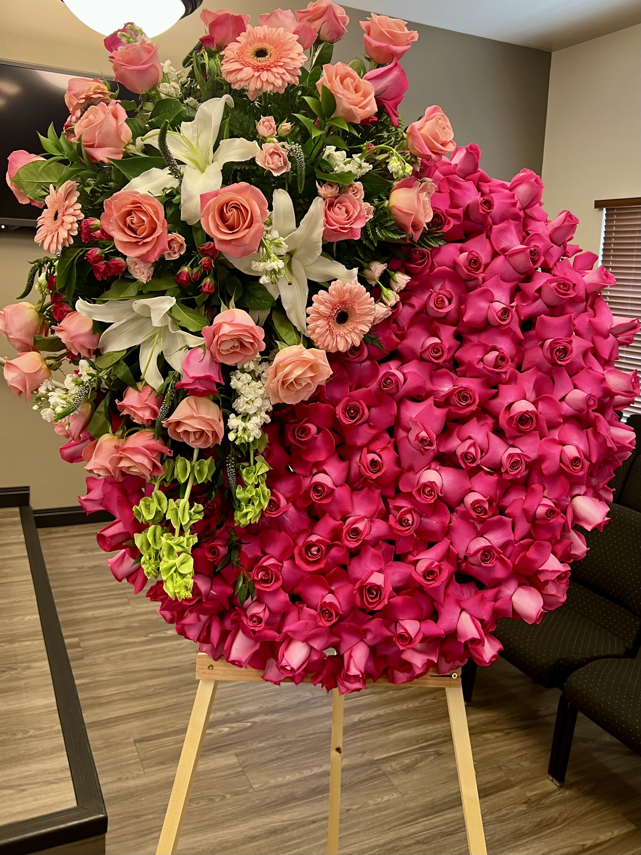 Large circular standing spray of hot pink roses with peach blooms and white lilies on a wooden easel