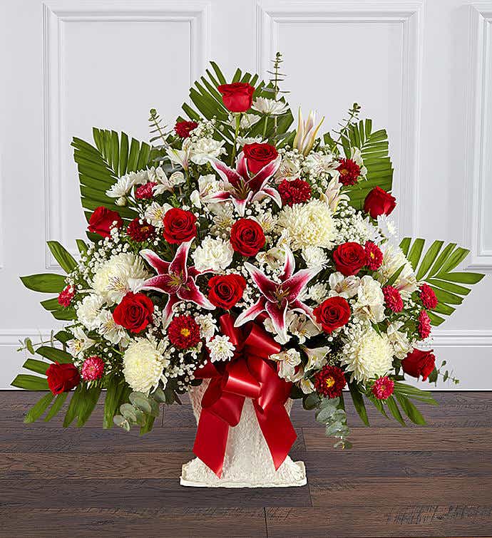 Large red and white flower arrangement with lilies and roses in a white urn with red ribbon