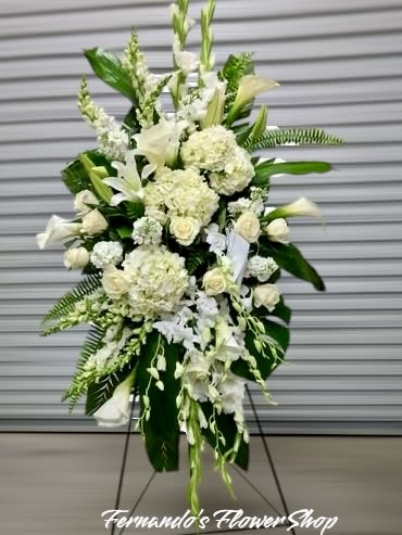 Tall white standing spray of mixed flowers and large tropical leaves on an easel.