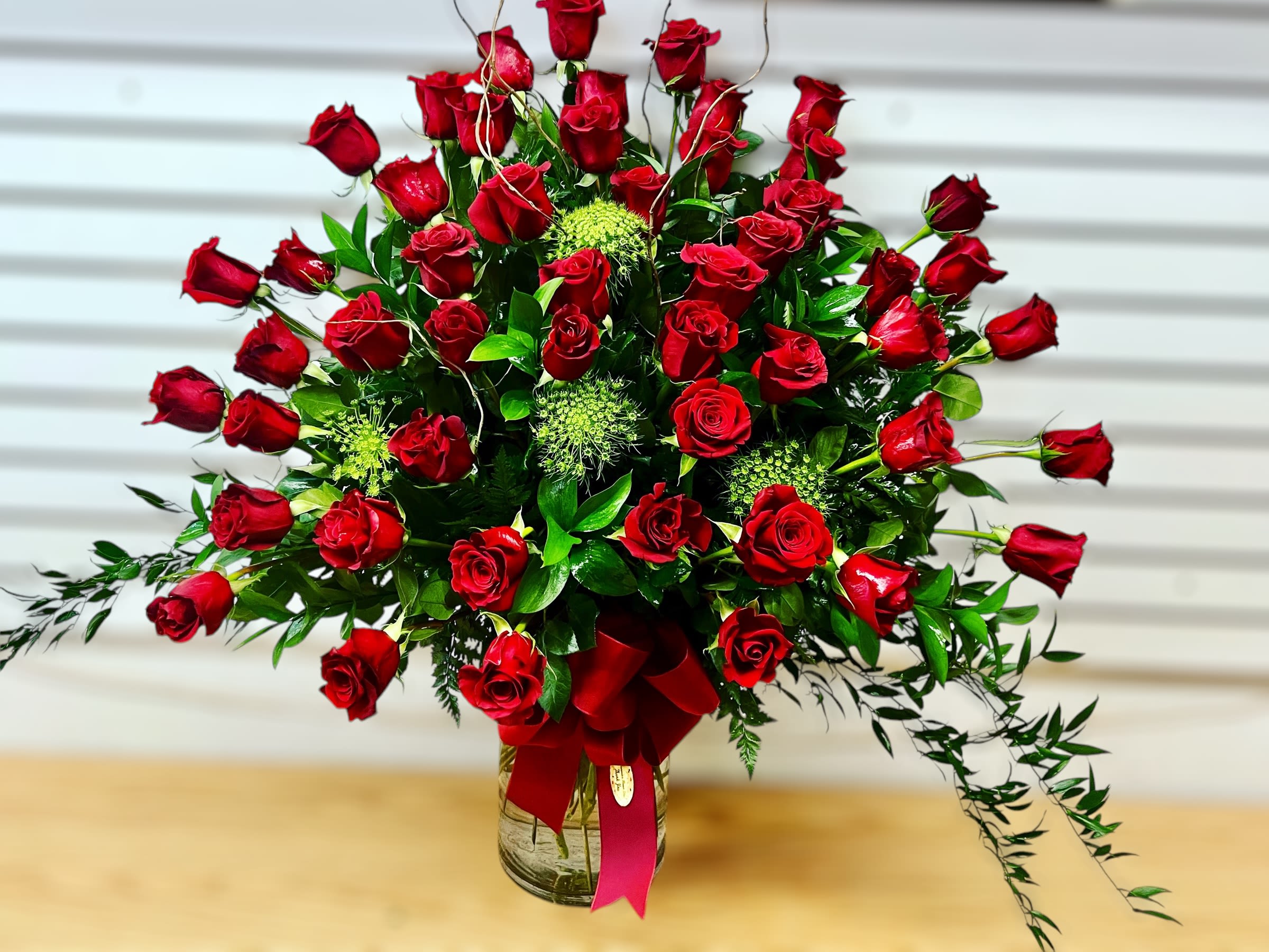 Large fan-shaped arrangement of red roses in a clear glass vase with a red bow.