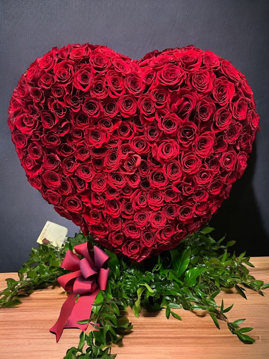Heart-shaped arrangement of tightly packed red roses with a red ribbon bow at the base