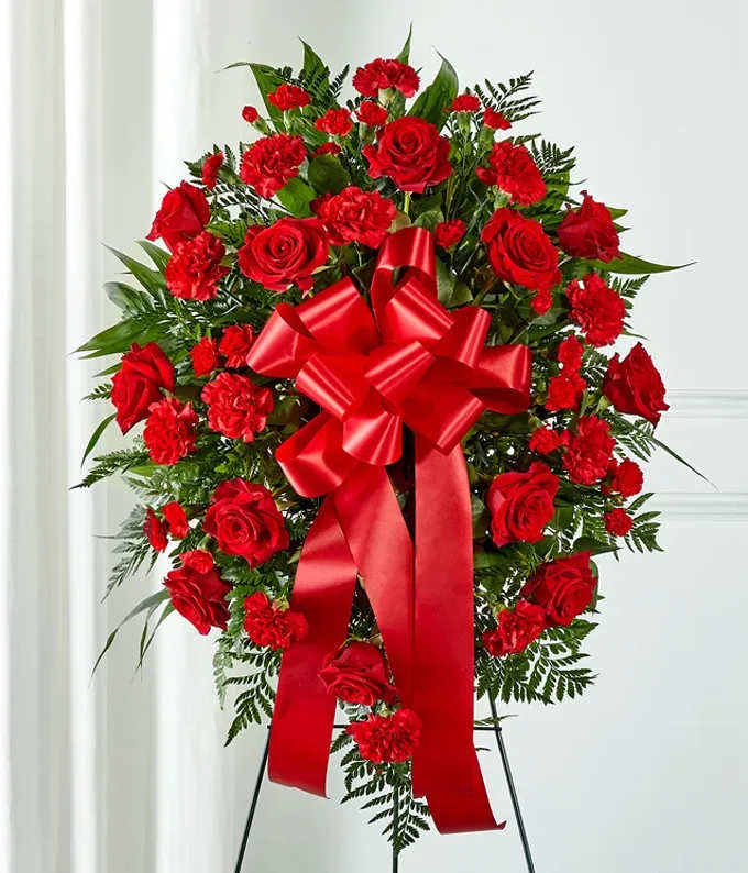 Standing spray of red roses and carnations with a large red bow on an easel
