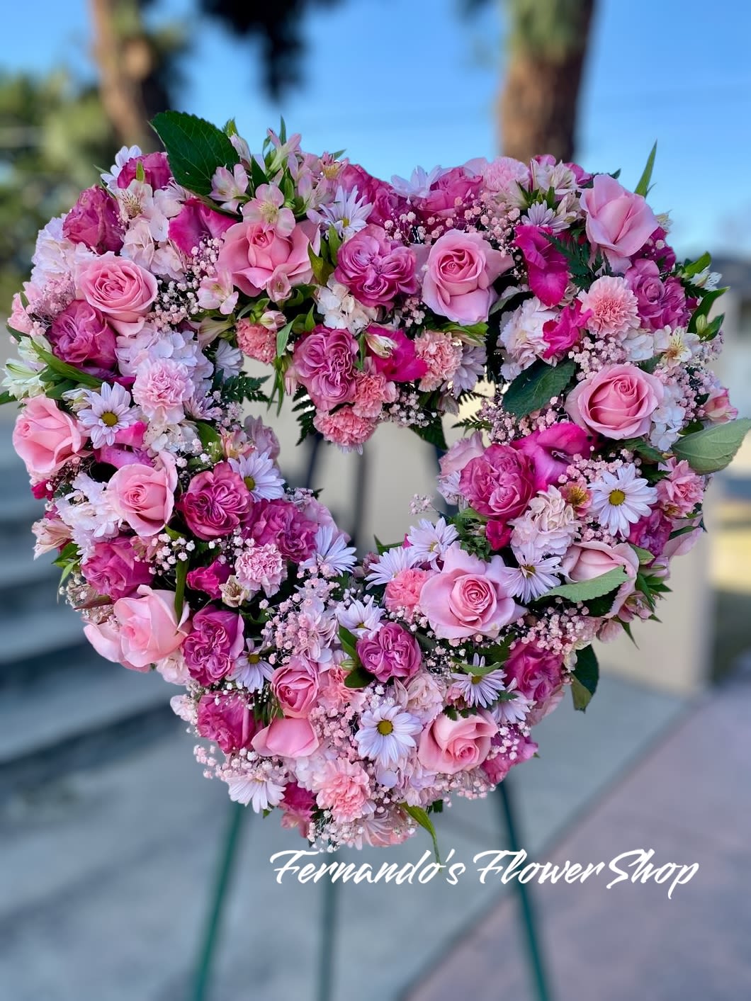 Heart-shaped standing wreath of pink roses, carnations, and daisies on an easel