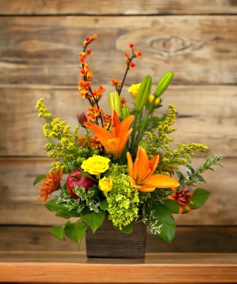 Apples &amp; Lilys - A Warm &amp; Vibrant Floral Arrangement   Brighten up any space with this stunning arrangement featuring bold orange lilies, cheerful yellow roses, delicate greenery, and unique seasonal accents. Nestled in a rustic wooden box, this design exudes warmth, elegance, and a touch of nature’s beauty—perfect for any occasion!   