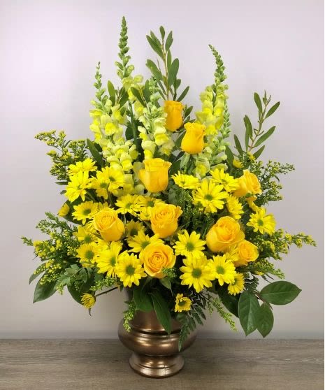 Tall yellow arrangement with roses, daisies, and snapdragons in a bronze urn vase
