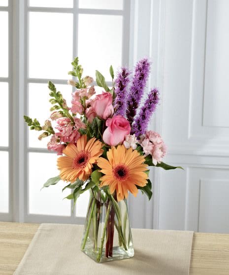Mixed bouquet of orange gerbera daisies, pink roses, and purple spikes in a clear glass vase