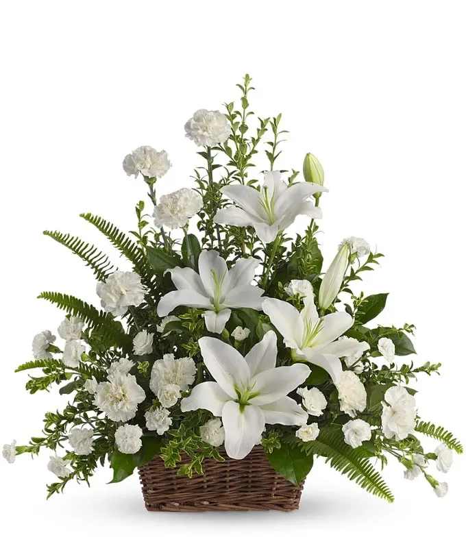 White lilies and carnations arranged in a wicker basket with abundant foliage