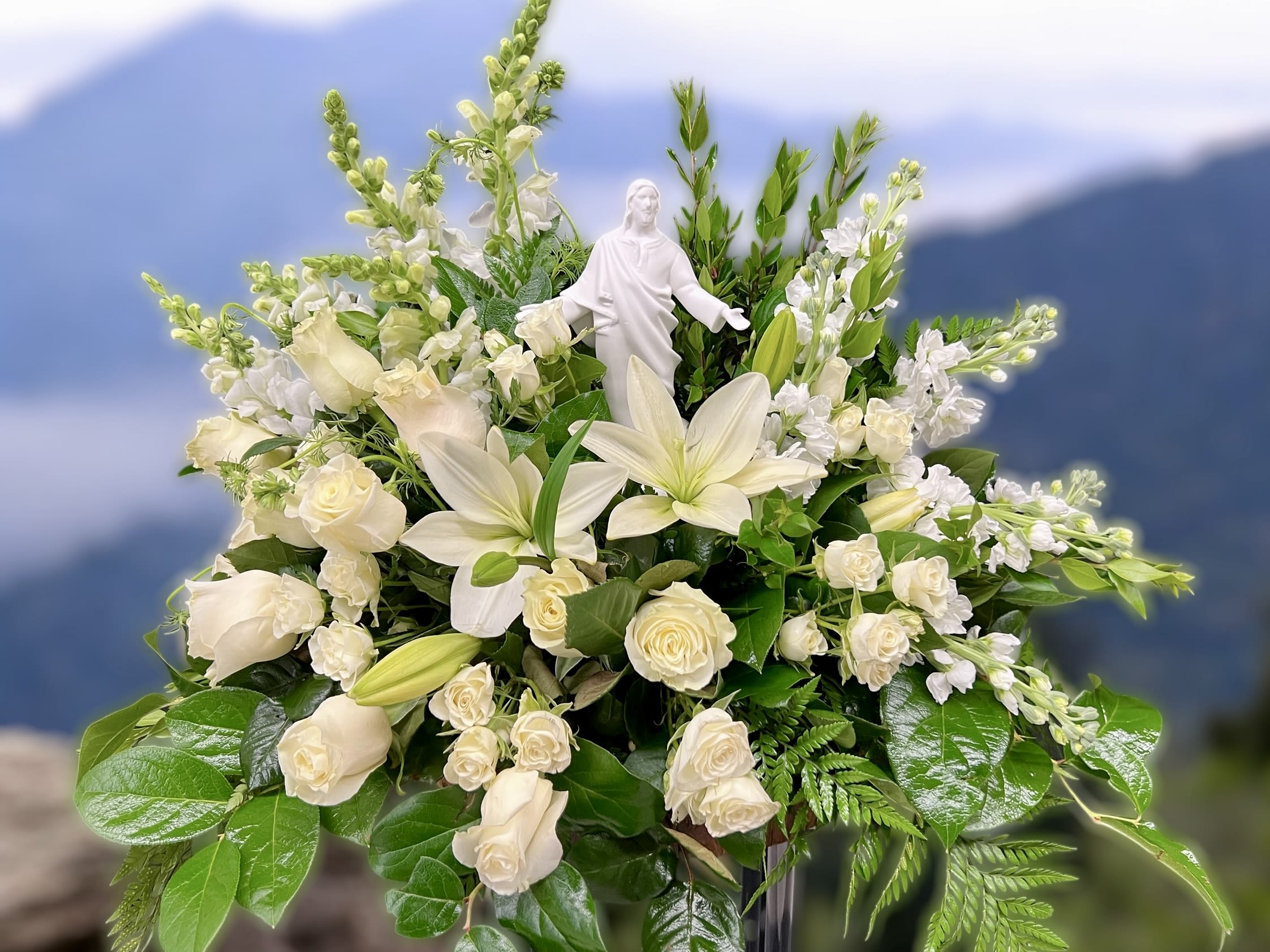 White lilies and roses arranged around a white religious figurine