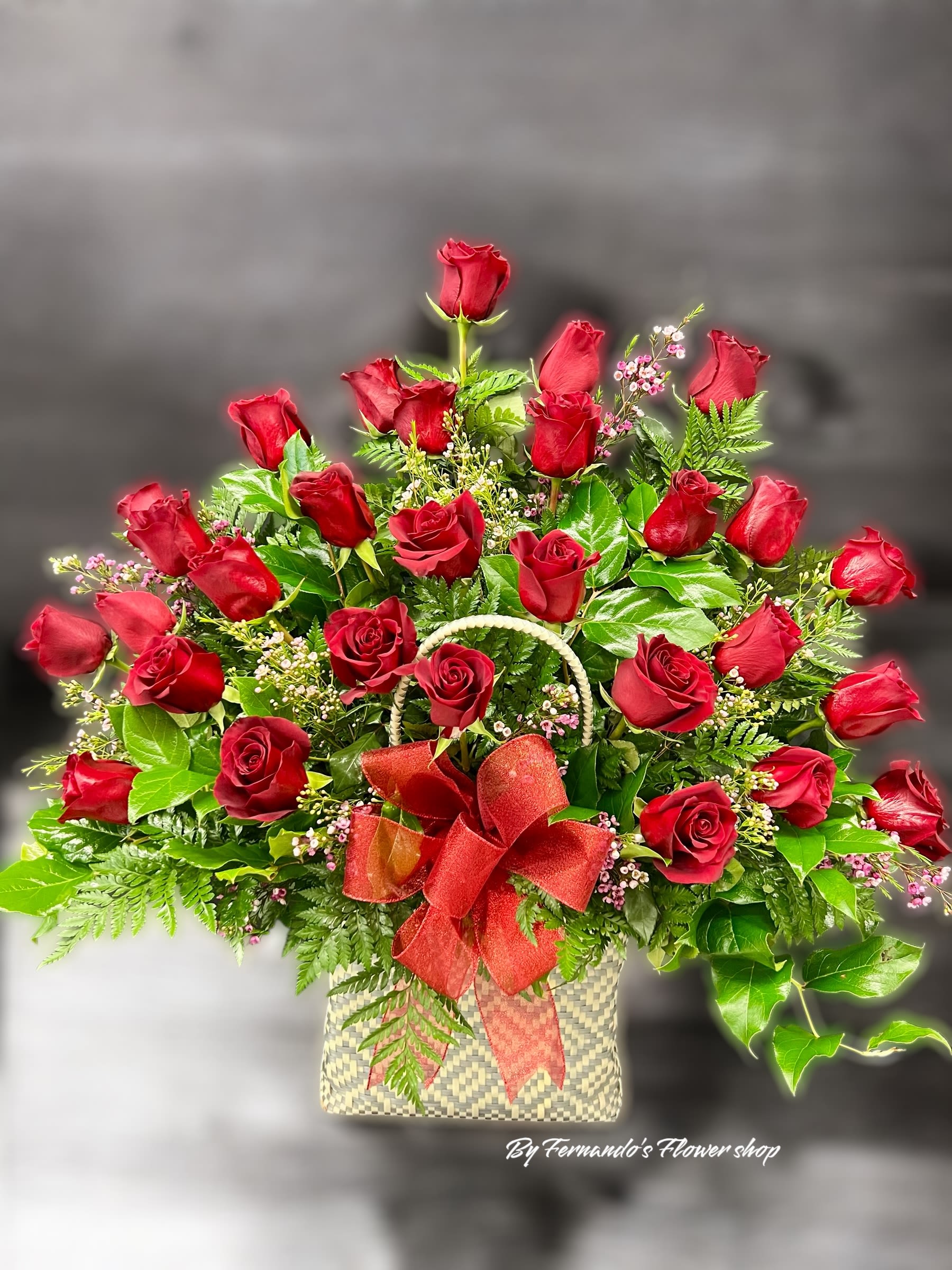 Large arrangement of red roses in a woven basket with a red bow