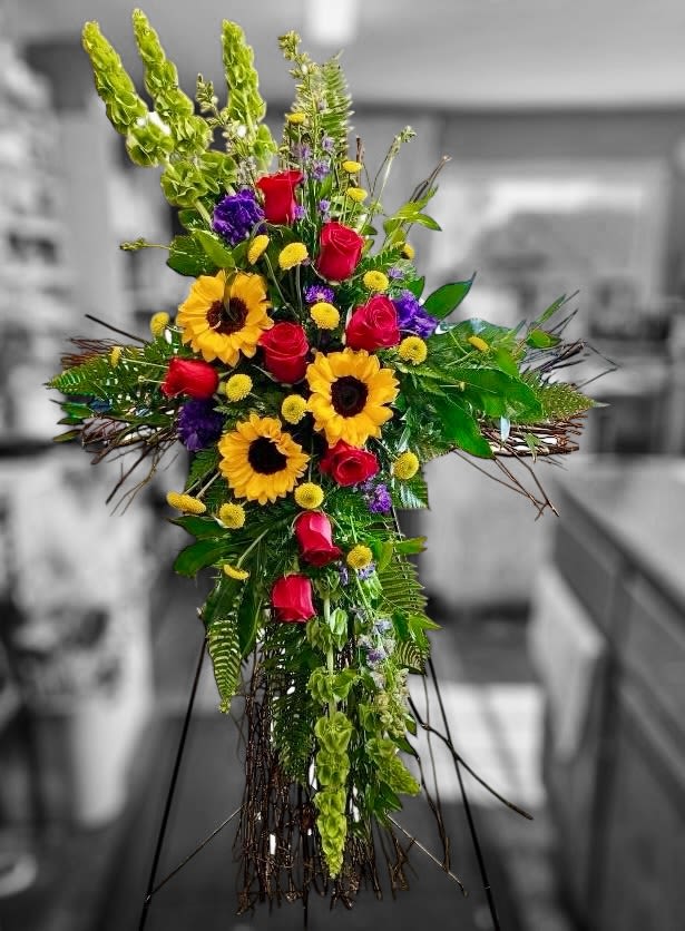 Tall cross-shaped standing spray with sunflowers, red roses, and yellow accents on an easel.