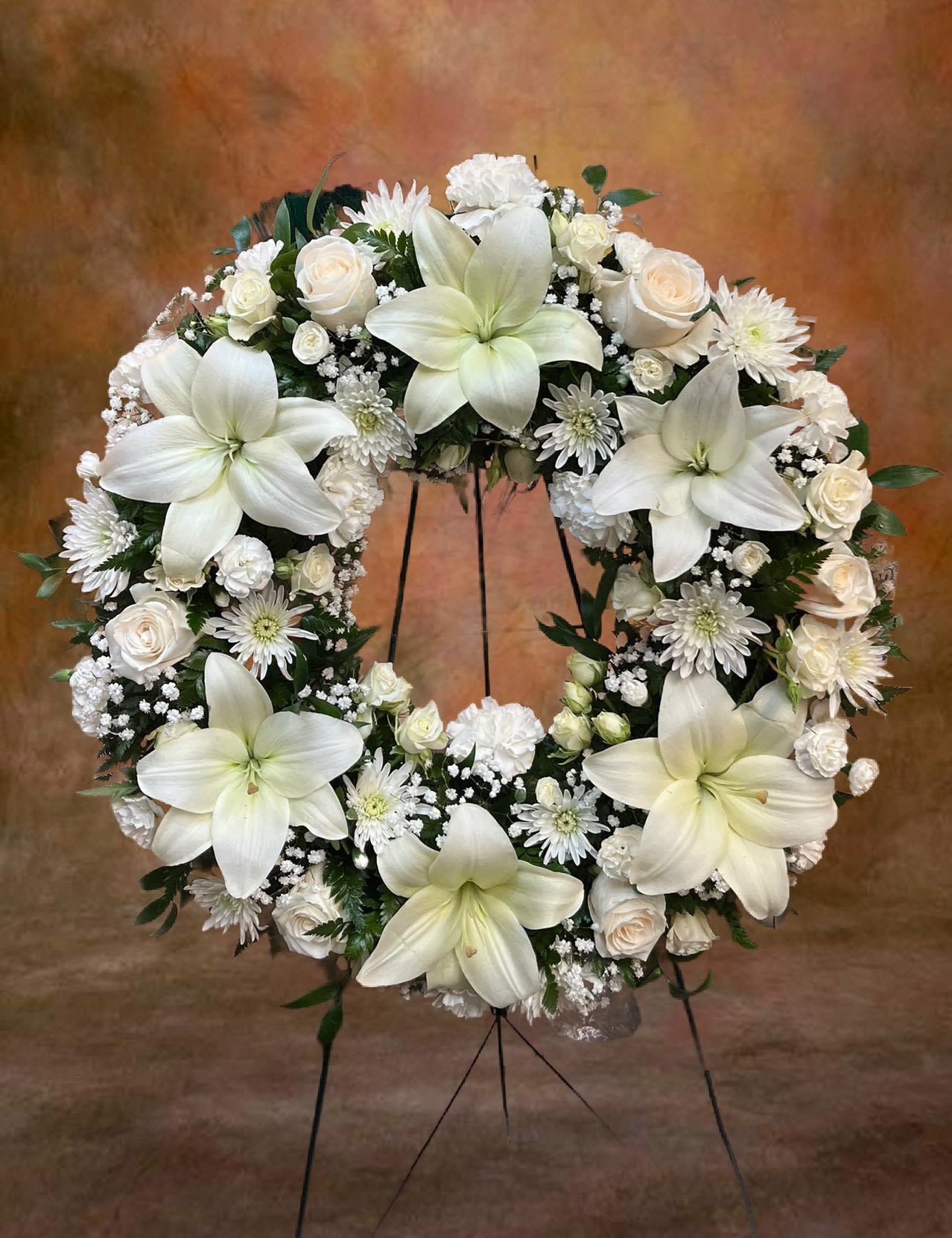 Standing wreath of white lilies, roses, and other white blooms on an easel stand