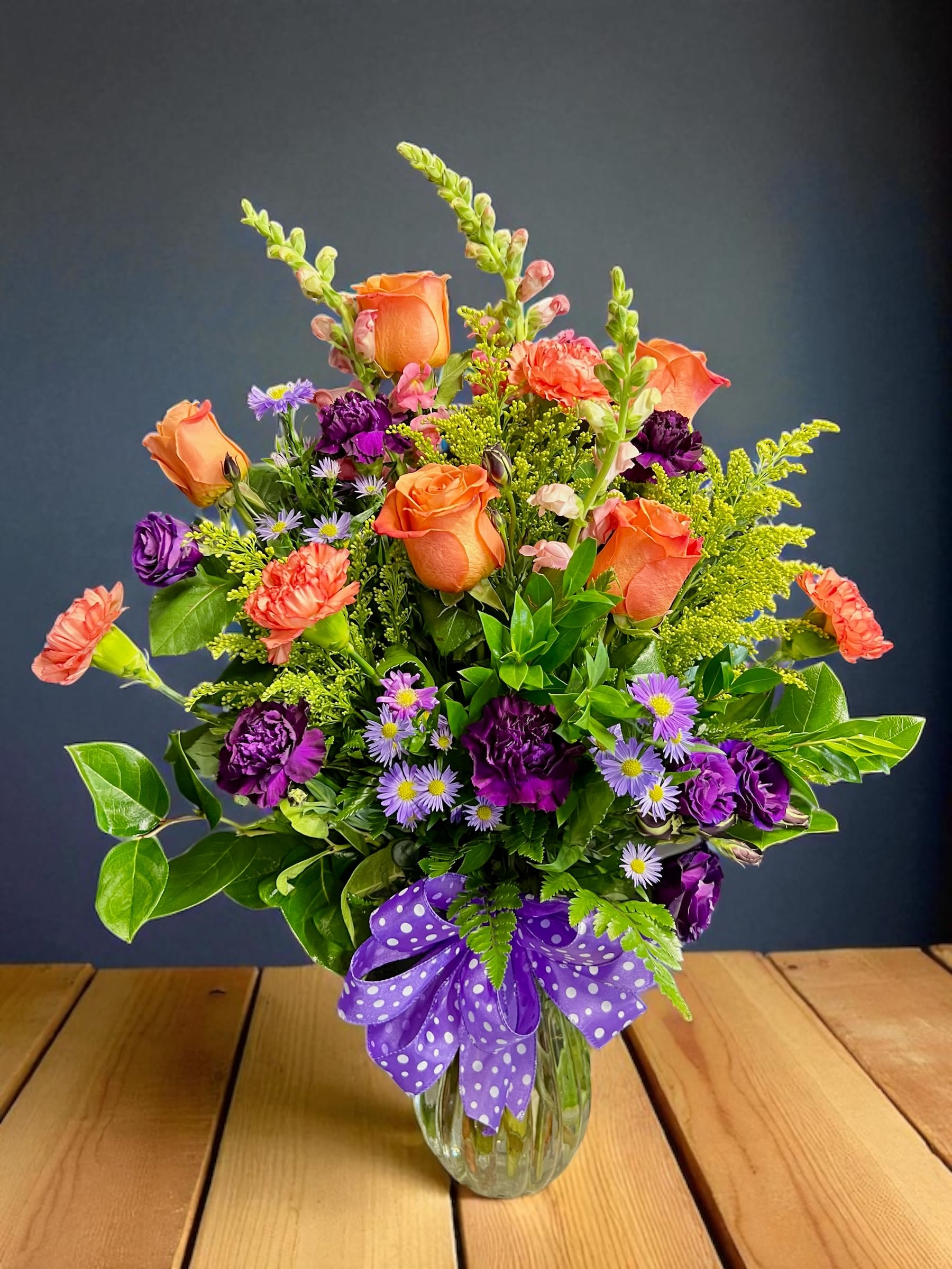 Mixed bouquet of orange and purple flowers in a clear glass vase with a purple bow.