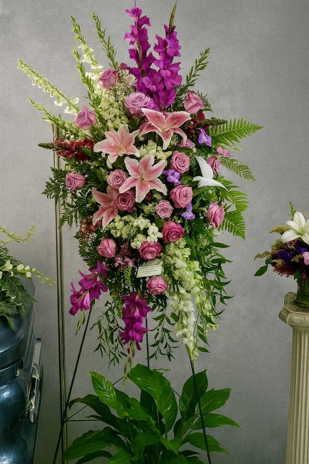 Tall pink and white standing spray with roses and lilies displayed on a metal easel