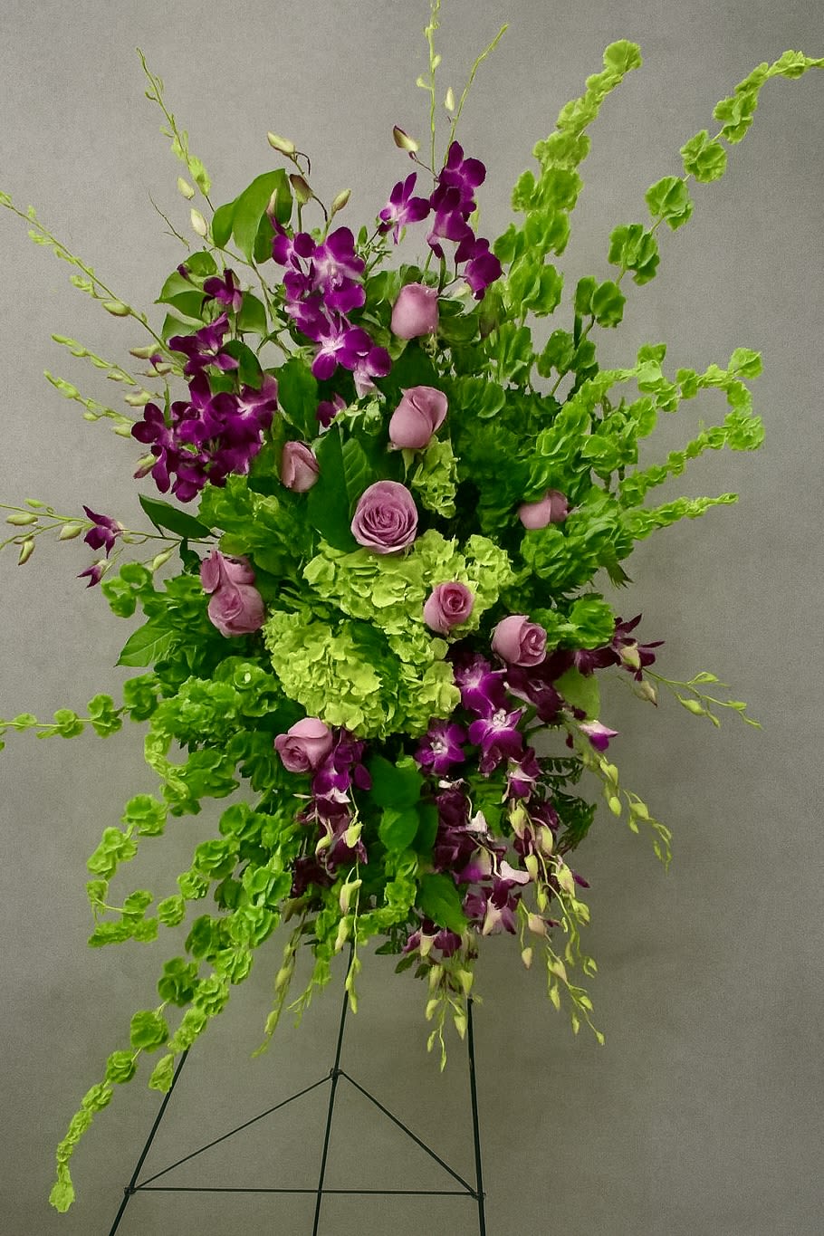 Tall standing spray of green hydrangeas, purple orchids, and pink roses on a metal easel