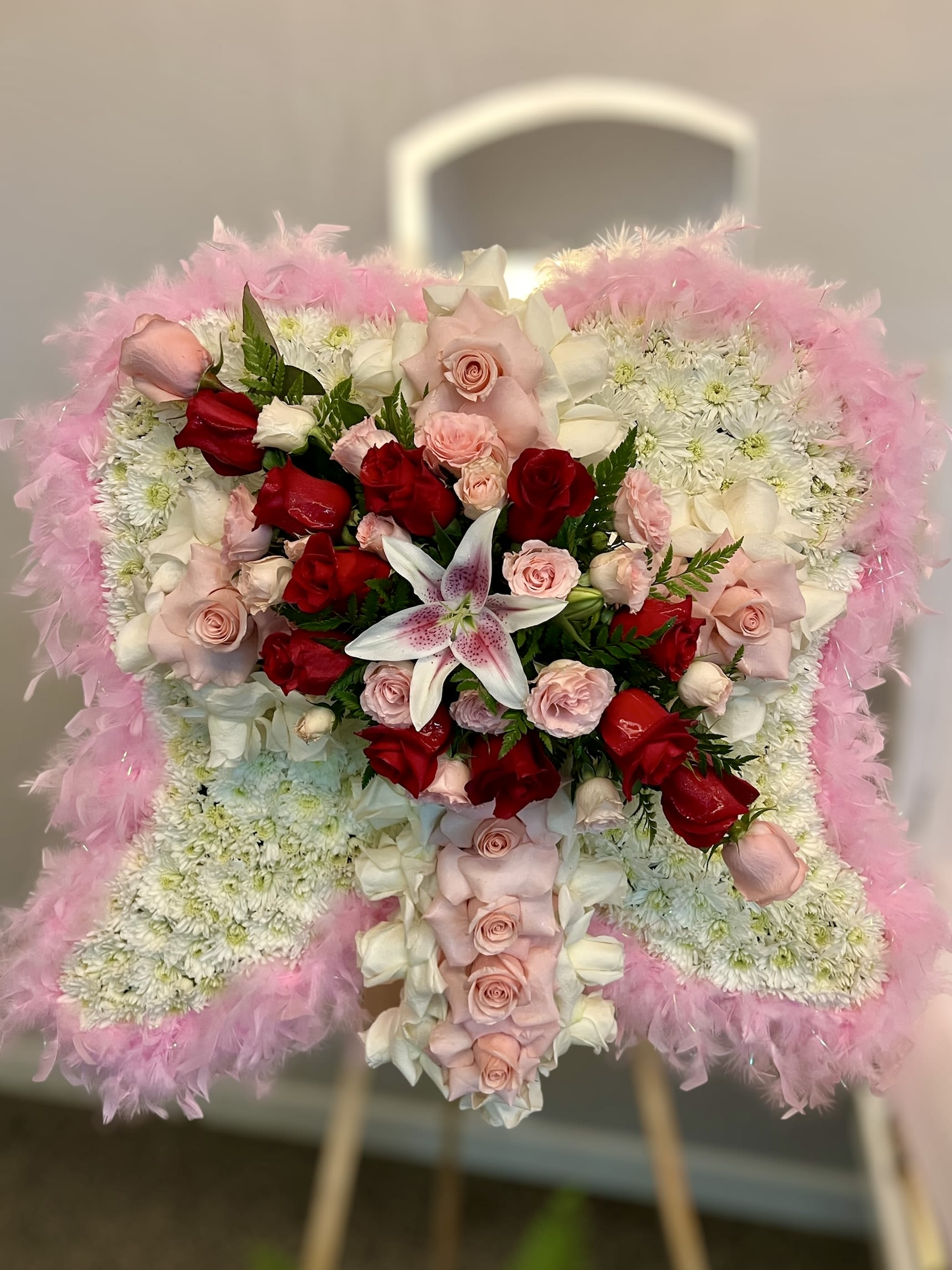 Standing angel-wing floral arrangement of white mums with pink feathers, roses, and a lily.