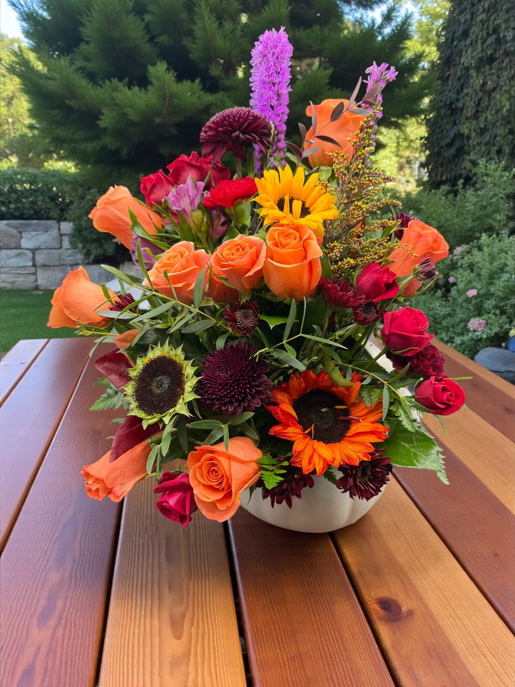 Mixed bouquet of orange and red flowers in a white bowl vase