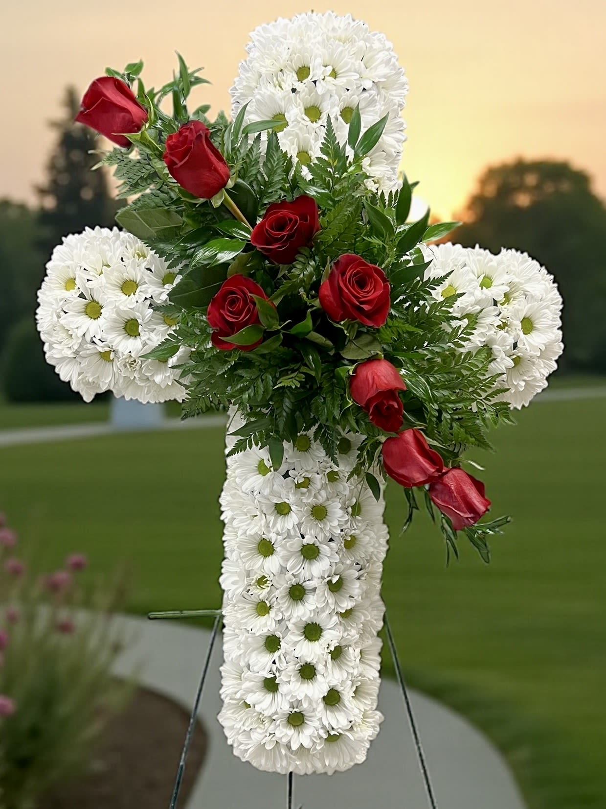 White floral cross with red roses on an outdoor stand