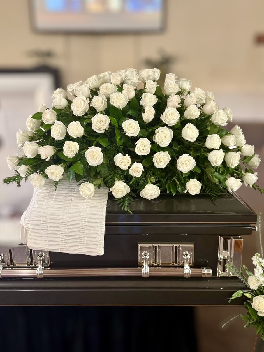 White rose casket spray on a dark casket with a white cloth drape