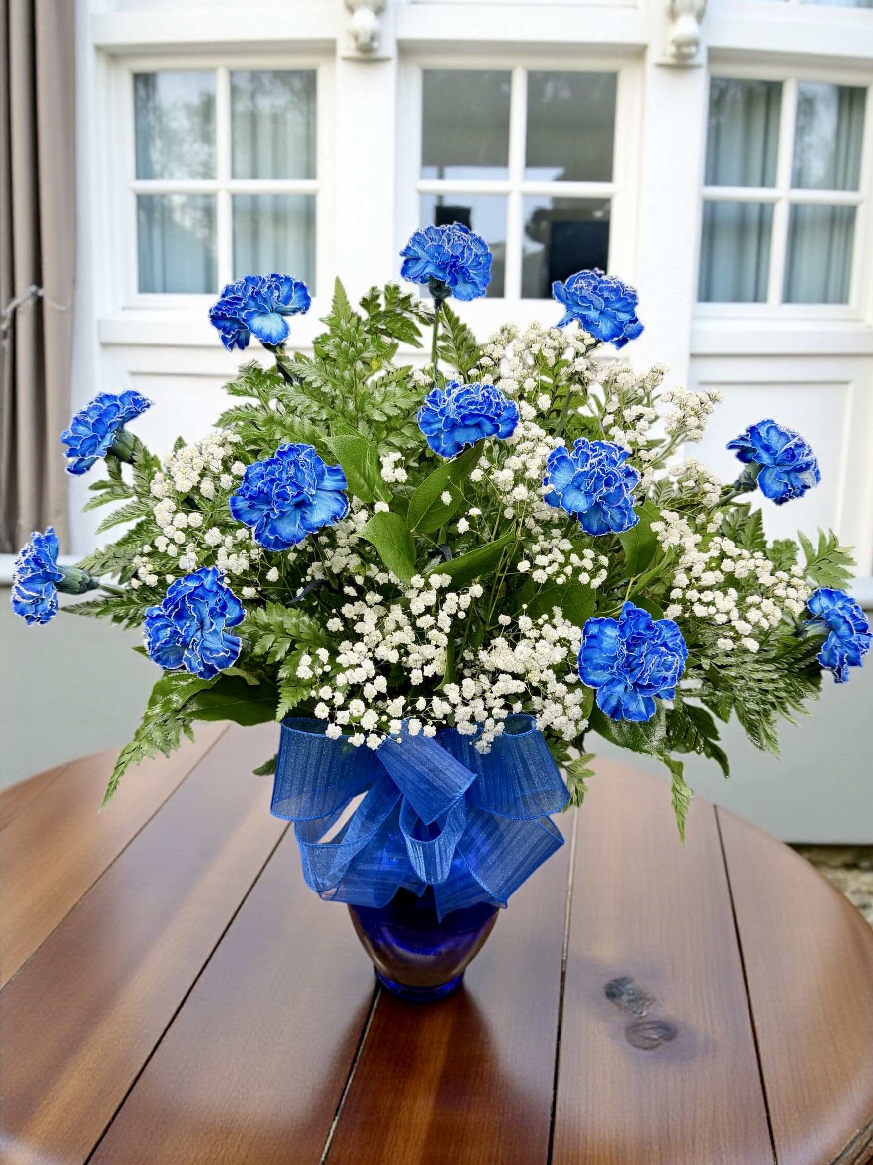 Blue carnations and white baby's breath in a glass vase with a blue ribbon