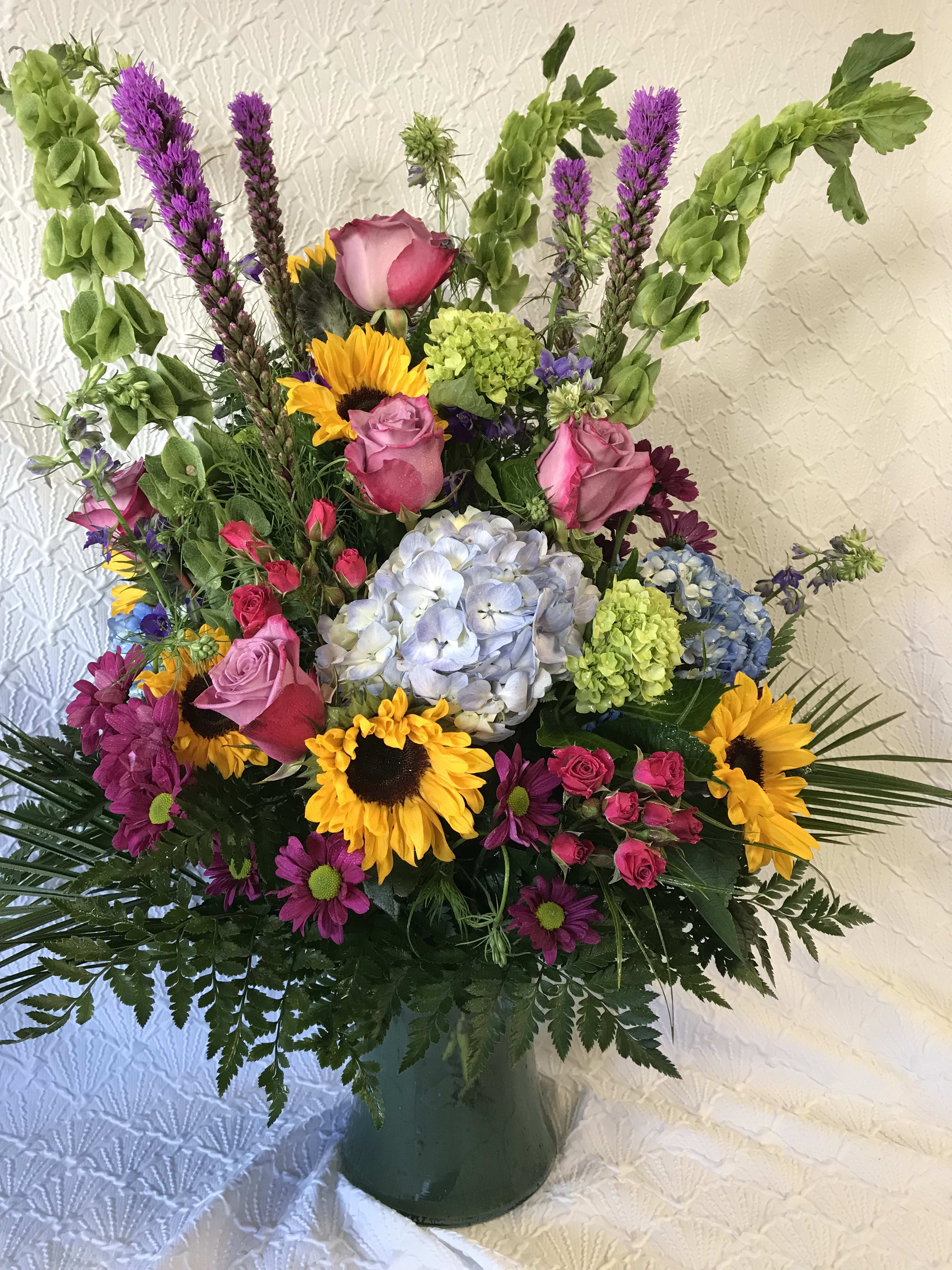 Mixed bouquet with sunflowers, roses, hydrangea, and purple spikes in a vase