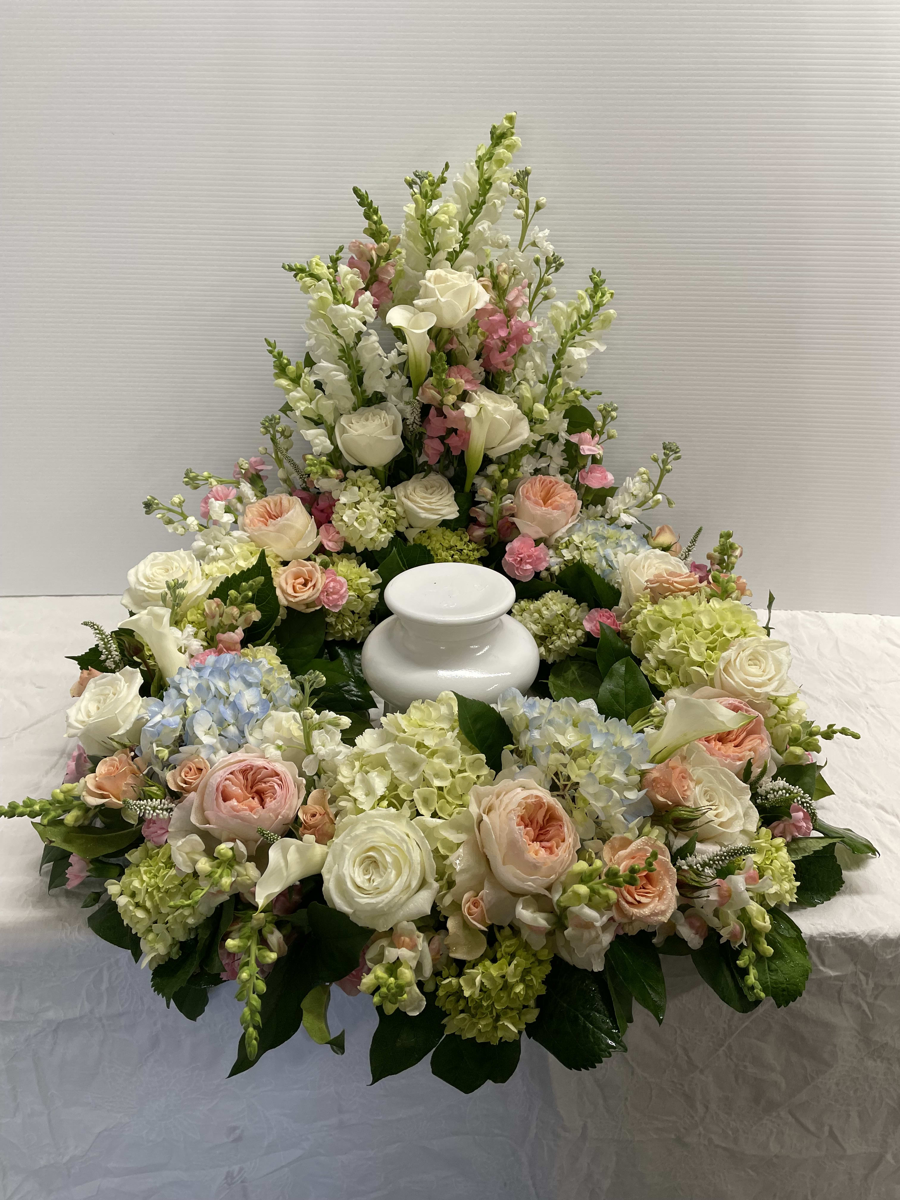 Large white and pastel floral funeral arrangement around a white urn