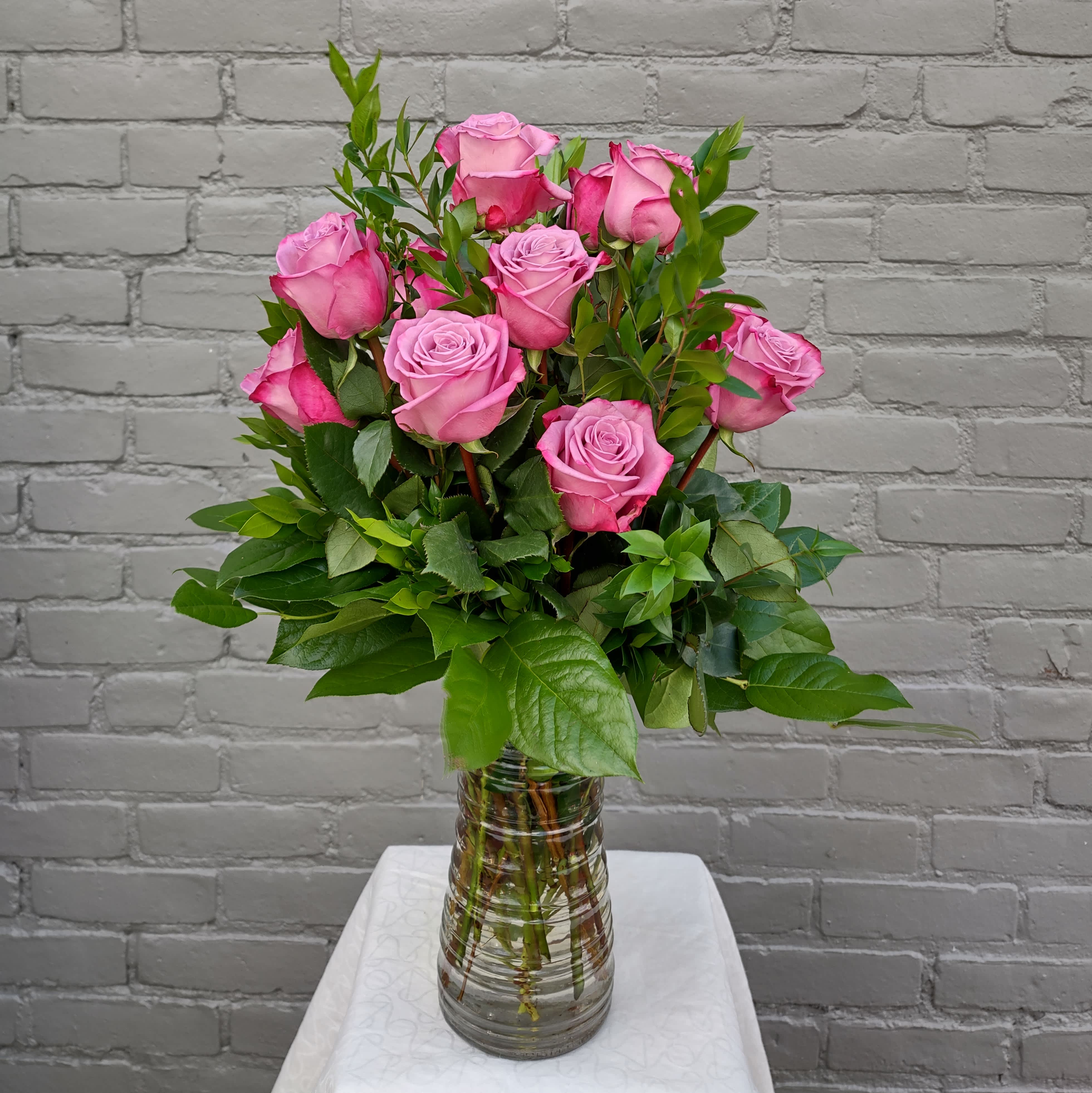 Lavender Rose Bouquet  - An enchanting bouquet of one dozen lavender roses sweetly touches their heart. Paired with lush greens in a glass vase these lovely roses are a perfect gift.