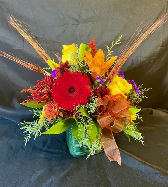 Bright mixed bouquet in a teal vase with a brown ribbon
