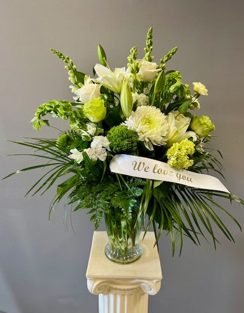 White and green sympathy arrangement in a glass vase with a "We love you" ribbon