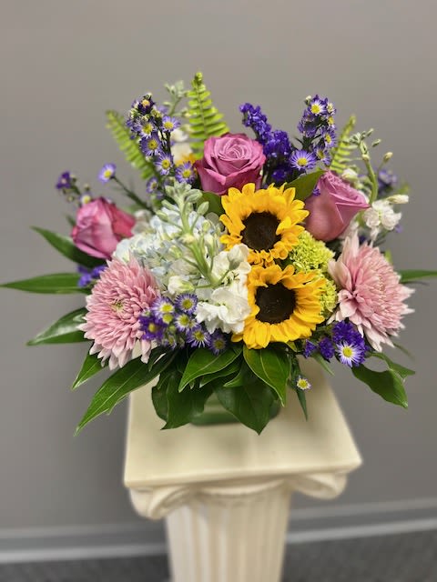Mixed bouquet with sunflowers, pink roses, and purple flowers in a vase