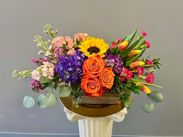 Colorful mixed flower arrangement in a wooden box on a pedestal