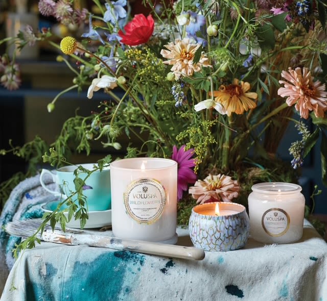 Wildflower arrangement with three lit candles and a turquoise cup on a painted cloth