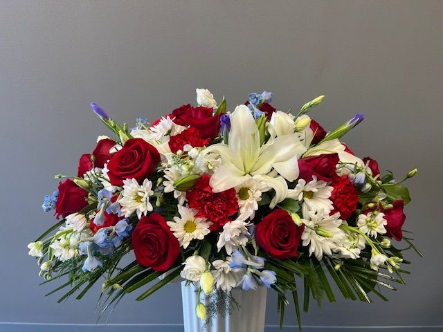 Red roses and white lilies in a white vase with small white and blue flowers
