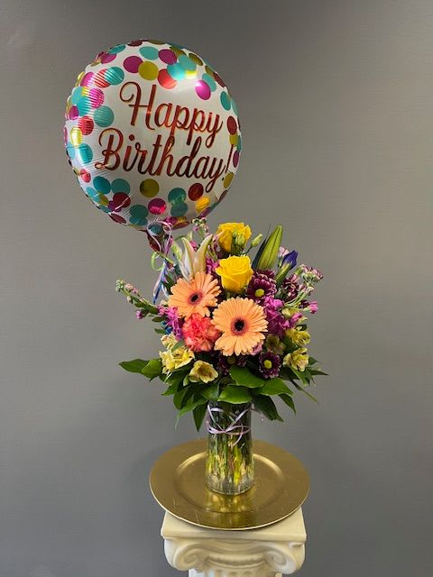 Birthday balloon above a mixed flower bouquet in a glass vase