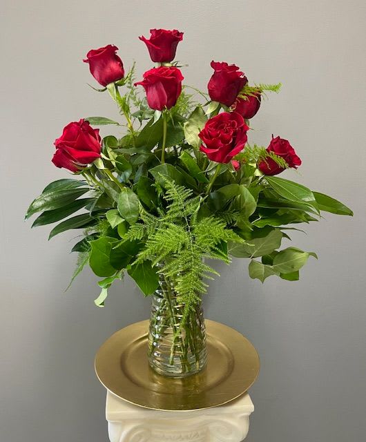 Red roses arranged in a clear glass vase with greenery