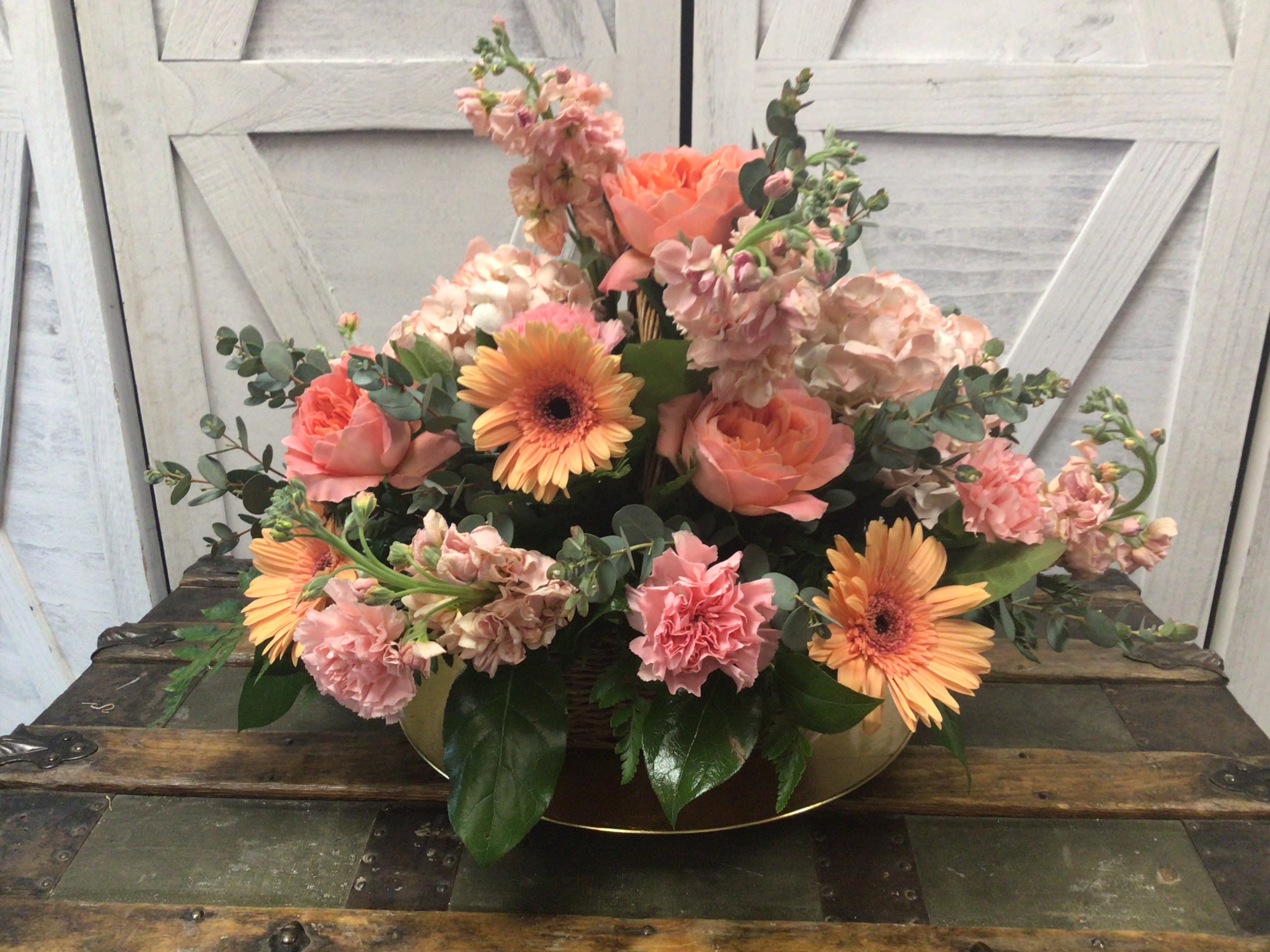 Coral Surprise - A brown wicker basket of seasonal wildflowers in shades of coral and peach.