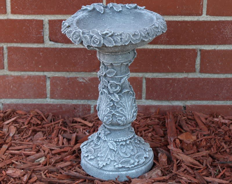 Decorative gray stone birdbath pedestal against a brick wall