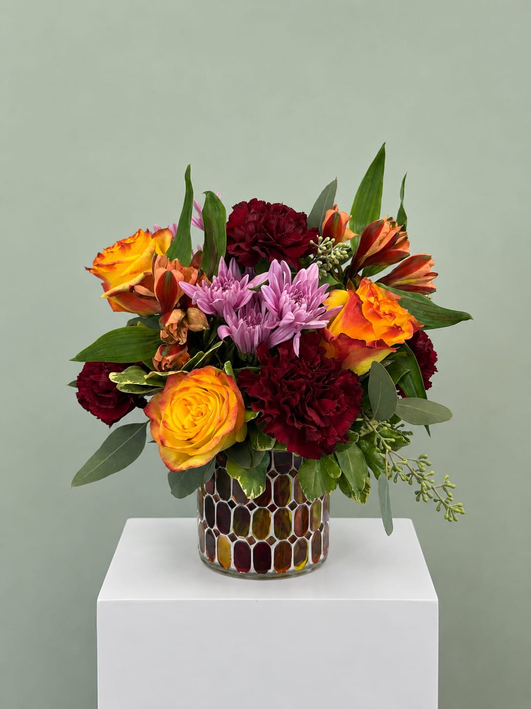 Mixed bouquet of orange roses, purple chrysanthemums, and burgundy carnations in a mosaic vase
