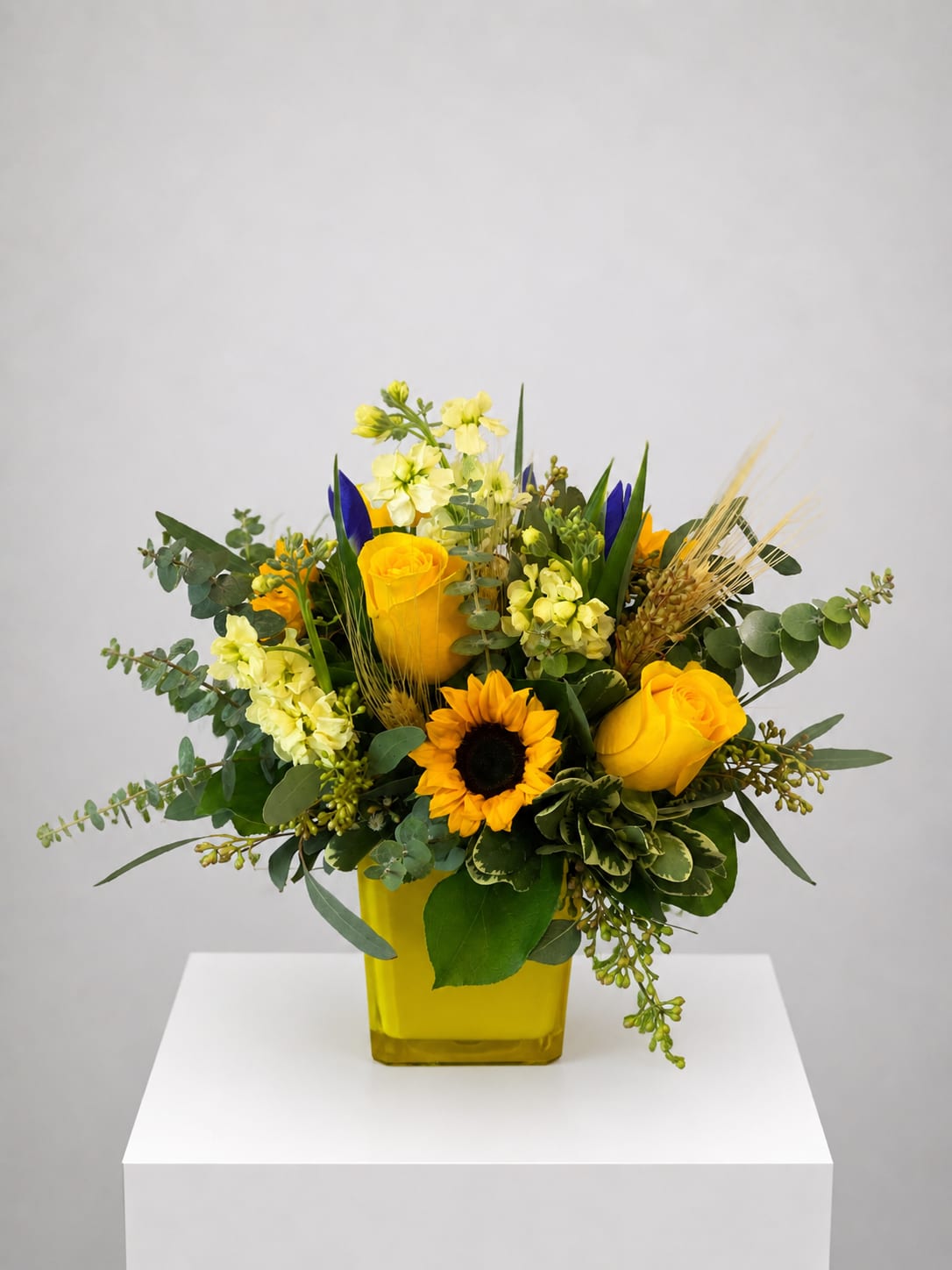 Yellow roses and a sunflower in a yellow vase with mixed greenery