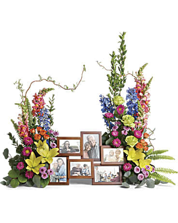 Two tall colorful floral arrangements framing a wooden multi-photo picture frame display.