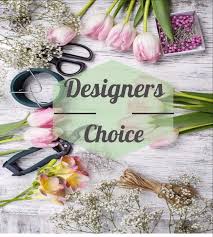 Pink tulips and floral tools arranged around a Designers Choice label on a wood surface