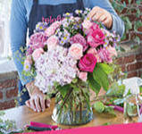 Round bouquet of pink and purple flowers in a clear glass vase on a table