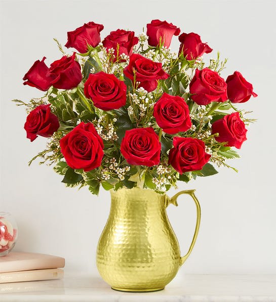 Arrangement of red roses with small white blooms in a hammered gold metal pitcher.