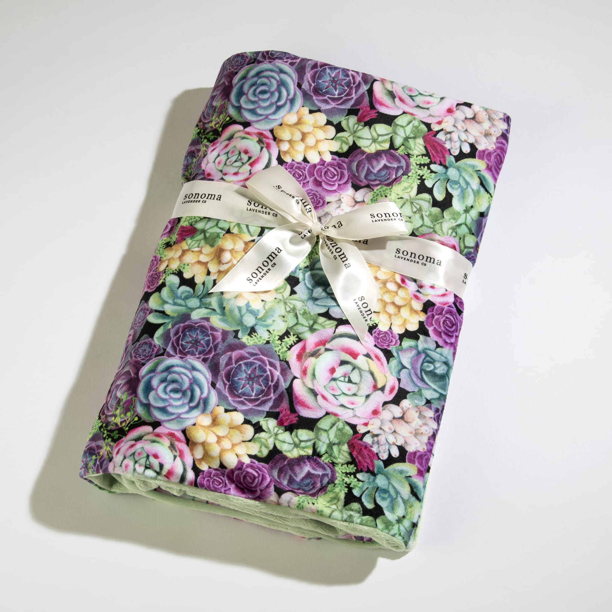 Folded blanket with colorful succulent pattern wrapped in a white Sonoma-branded ribbon