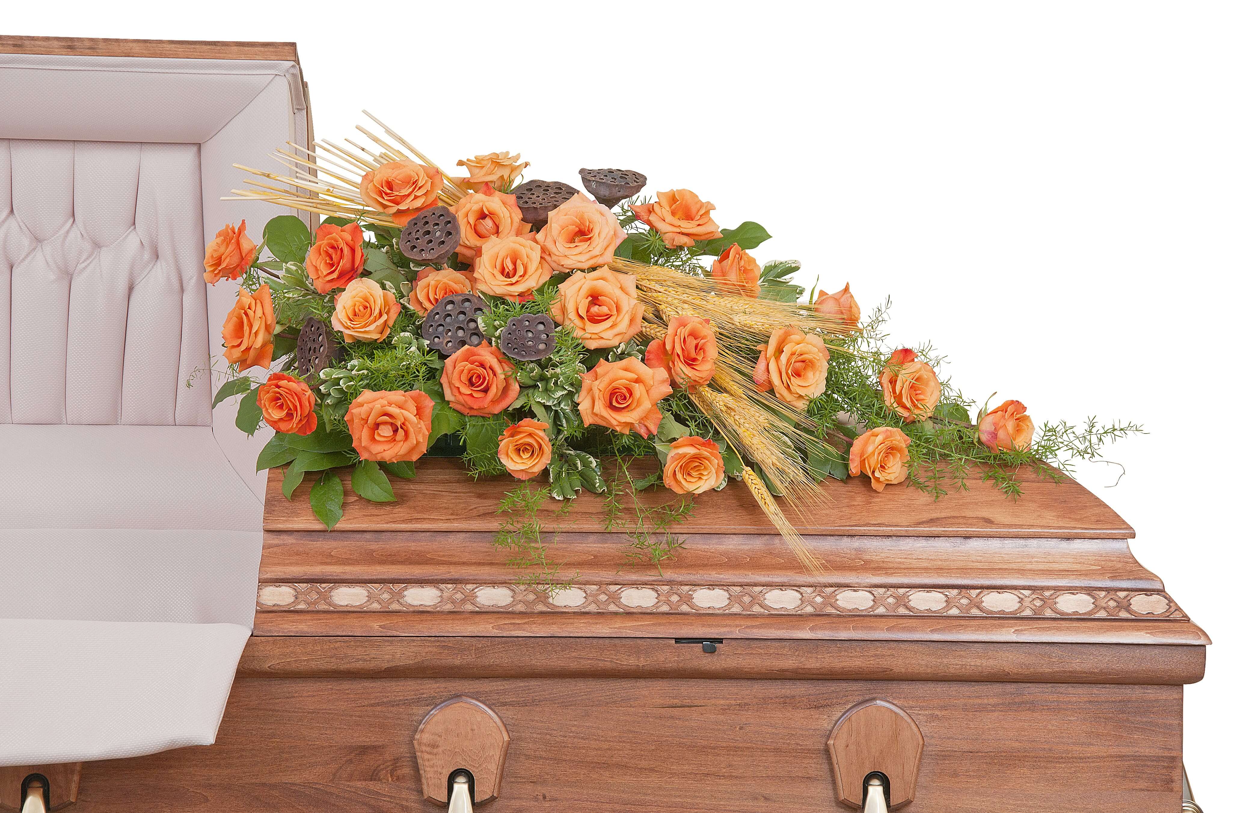 Orange rose casket spray with wheat accents arranged on a wooden casket