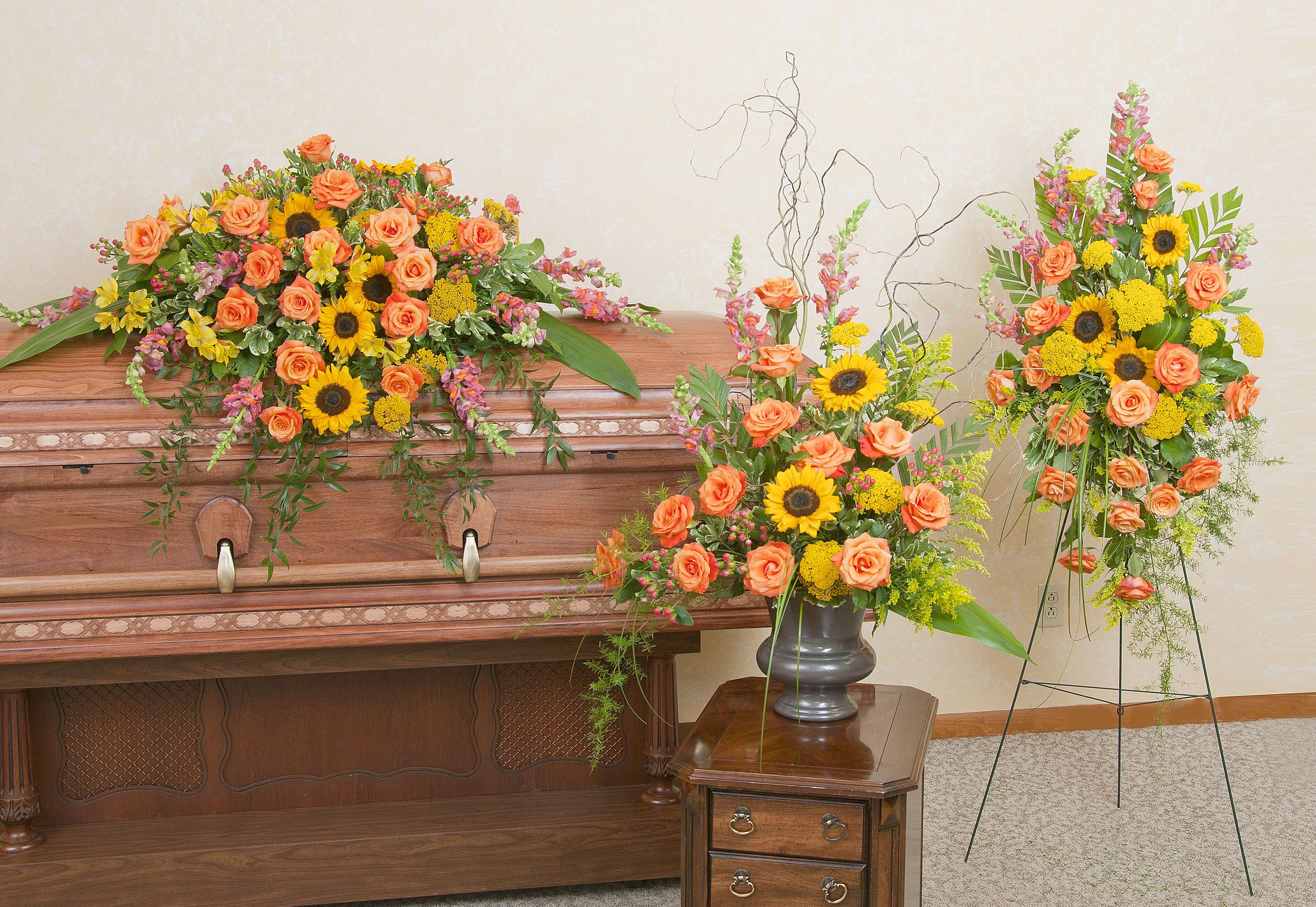Sympathy set with orange roses and yellow sunflowers on a casket, in a vase, and on a standing spray.
