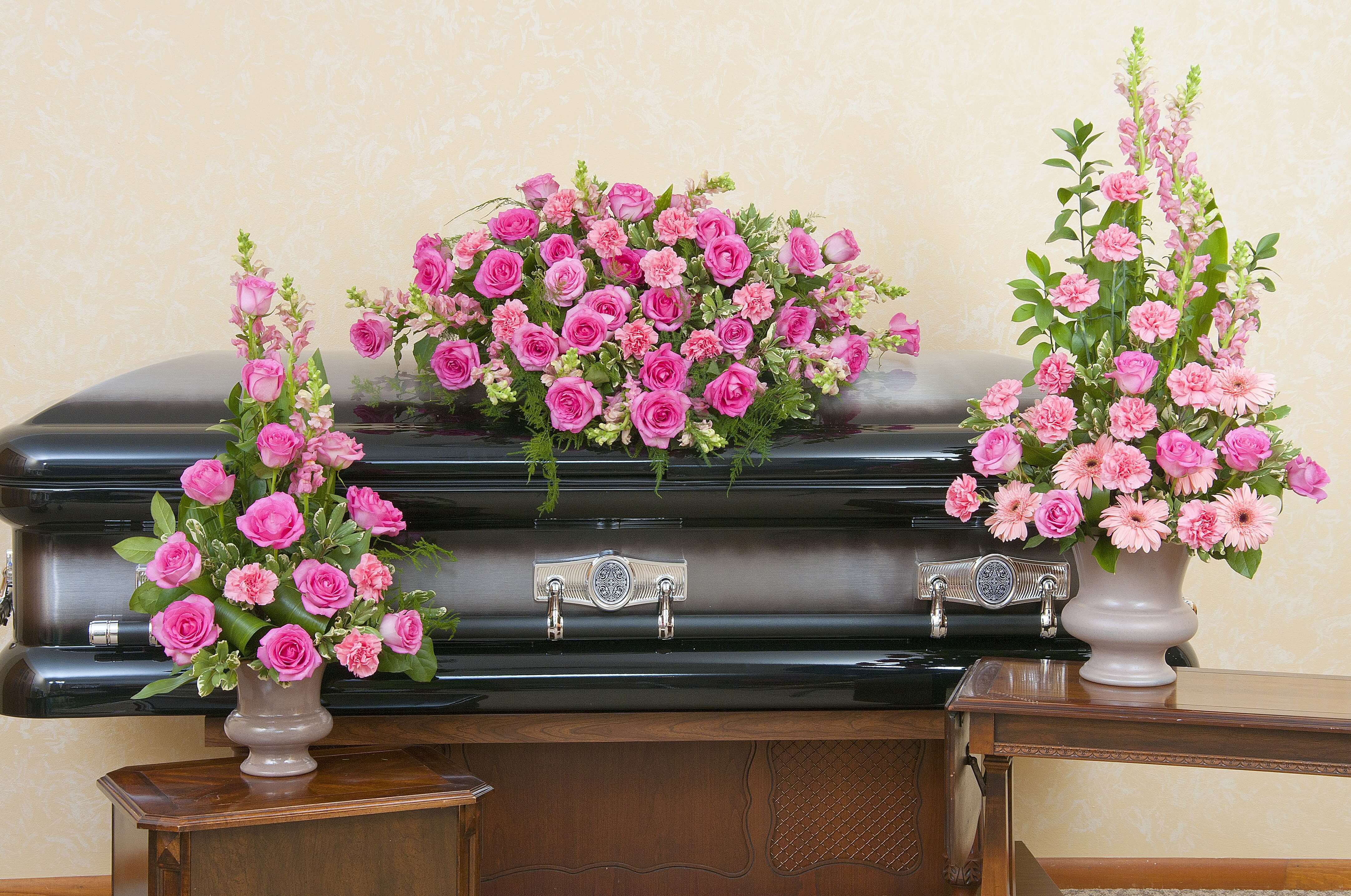 Pink rose and carnation casket spray with two matching standing arrangements on a dark casket