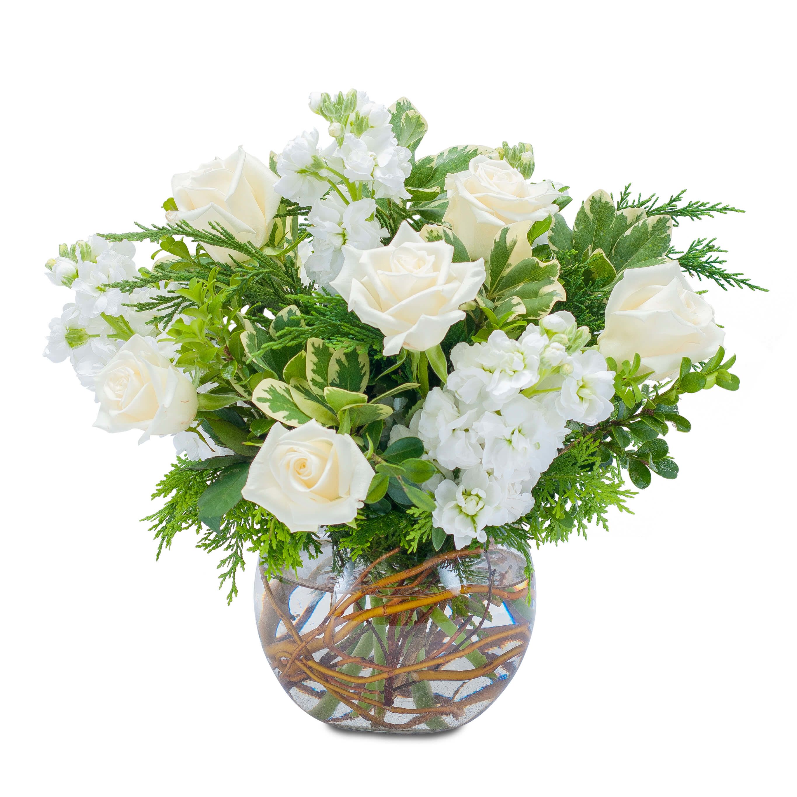 Low arrangement of white roses and stock in a clear glass bowl vase with curly branches in the water