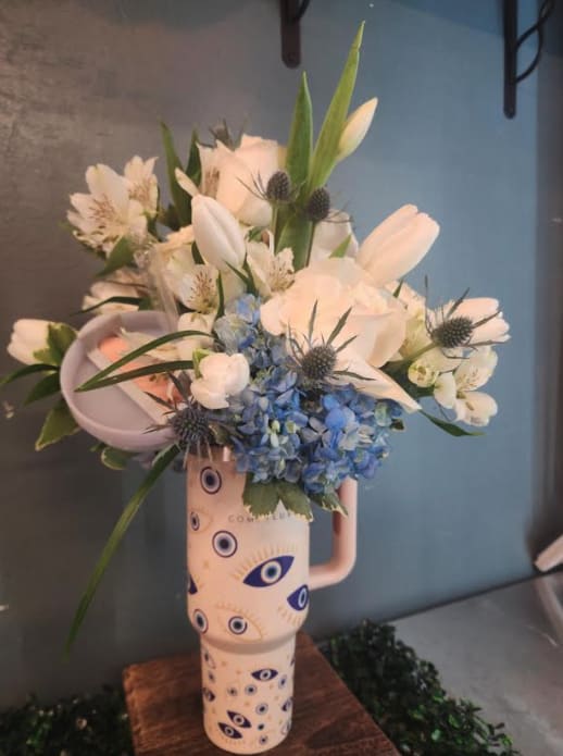 Tall arrangement of white and blue flowers in an evil-eye patterned ceramic tumbler