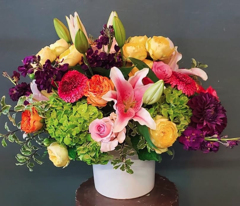 Colorful arrangement of lilies, roses, hydrangeas, and other blooms in a white ceramic vase