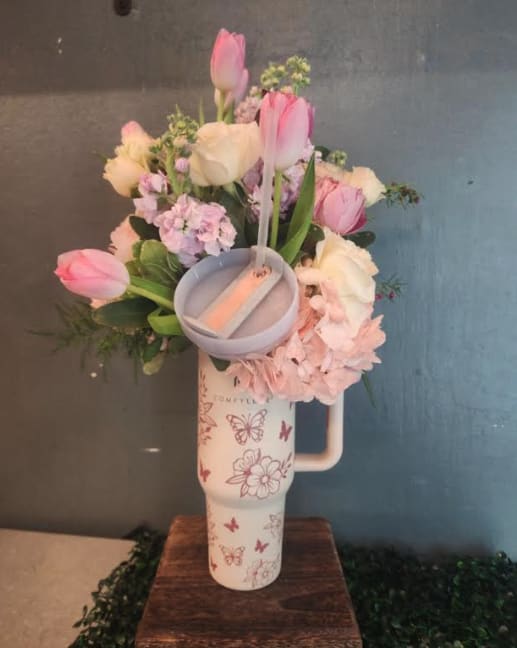 Pastel pink and white flower arrangement in a printed travel tumbler with a small candle on a wooden stand